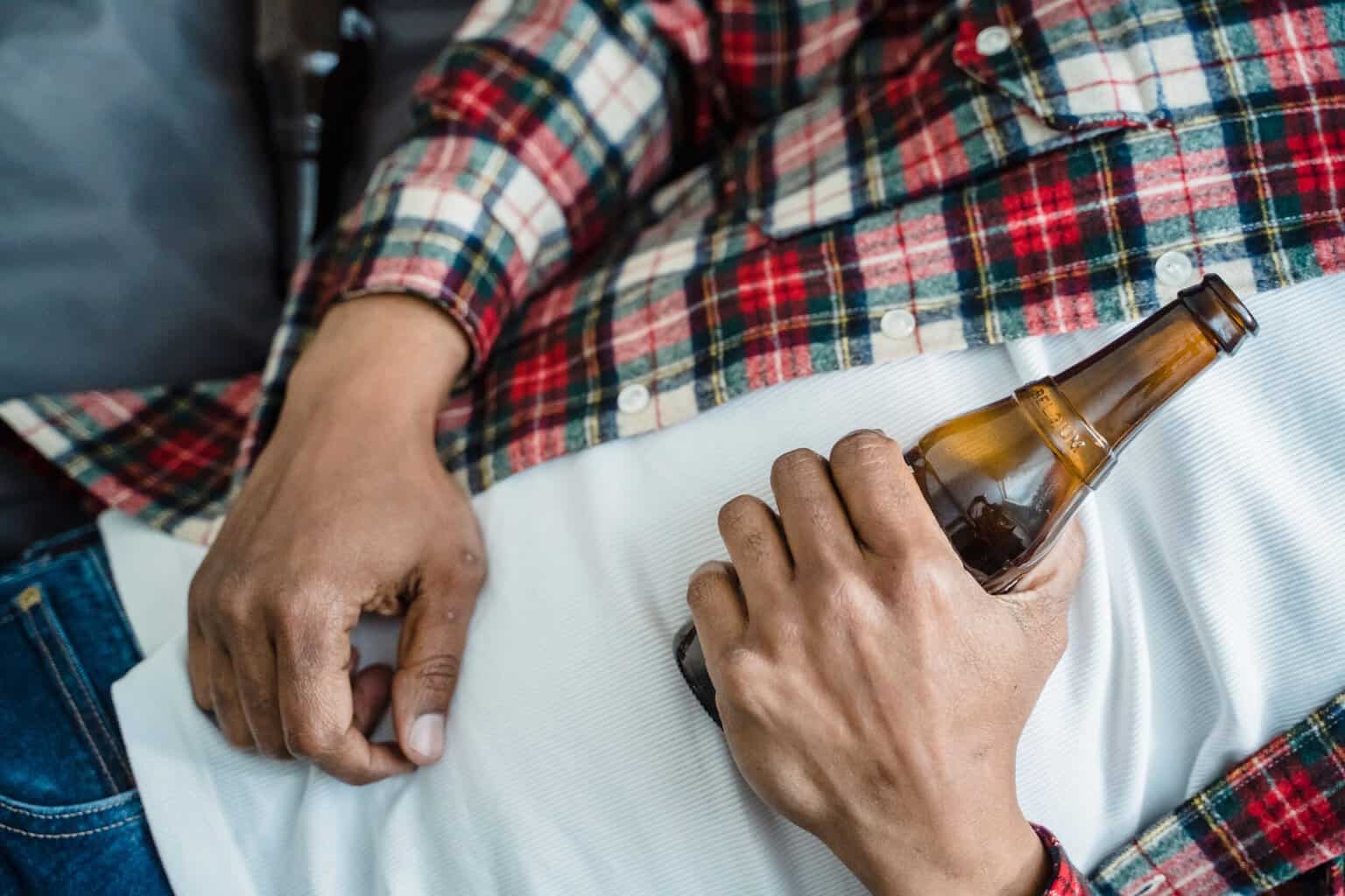 Close-up of a person lying down while holding a beer bottle, illustrating alcohol dependence and alcohol use disorder.