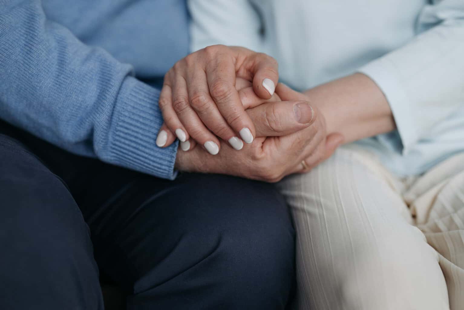 Close-up of one person holding another person’s hand in a supportive gesture, representing compassion and support during addiction recovery and treatment.